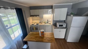 Une cuisine de taille réduite, dotée d’un plan de travail en bois, de meubles blancs, d’une cuisinière, d’un four à micro-ondes et d’un réfrigérateur.
