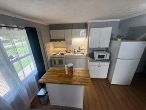 Une cuisine de taille réduite, dotée d’un plan de travail en bois, de meubles blancs, d’une cuisinière, d’un four à micro-ondes et d’un réfrigérateur.