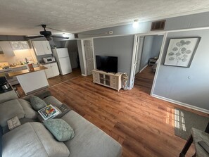 A modern living room with a sofa, a television, and a kitchen area in the background.