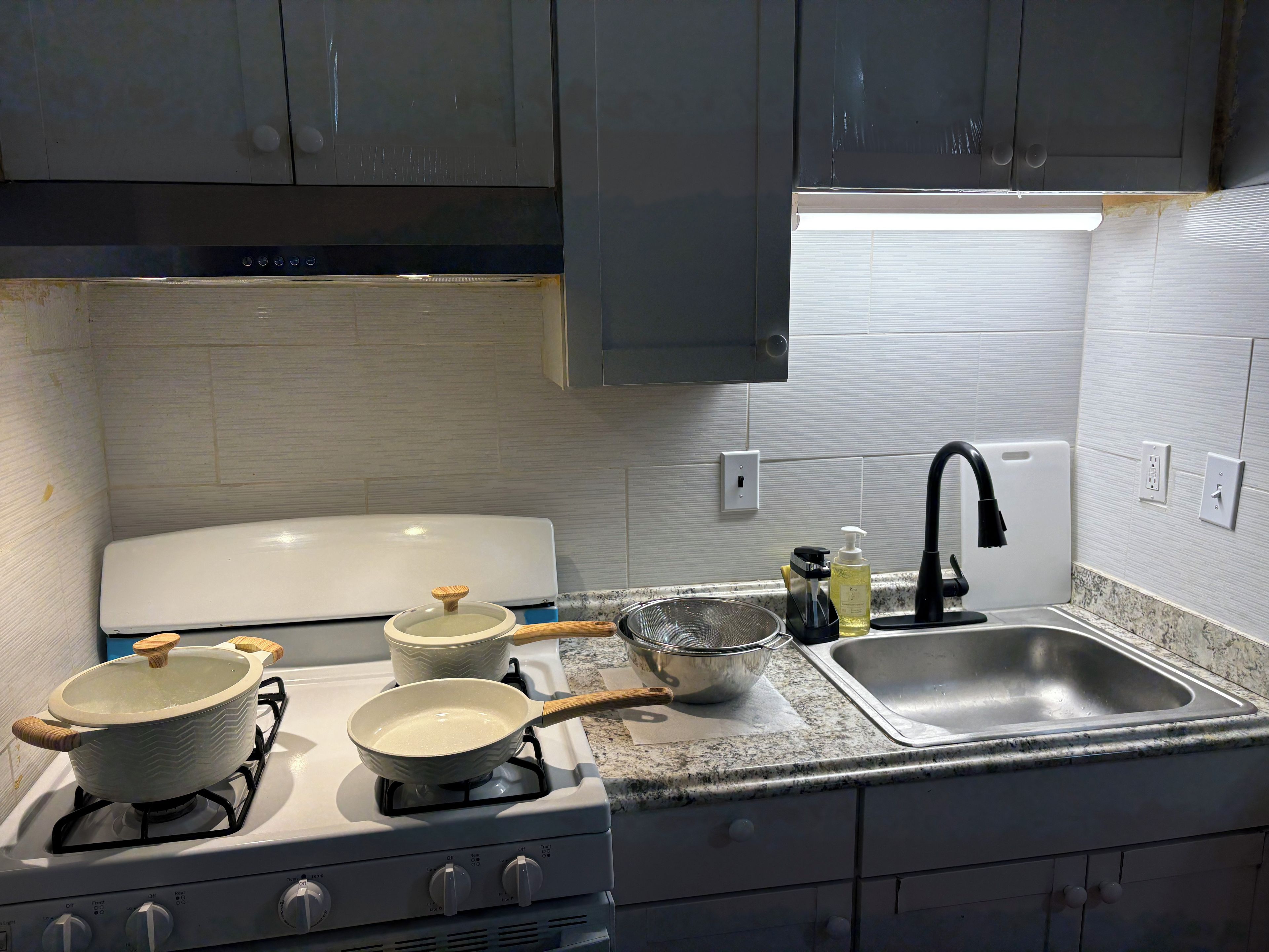 A kitchen with a gas stove, pots, a strainer, a sink, and a faucet.
