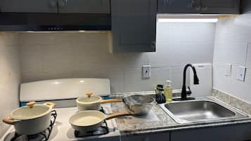 A kitchen with a gas stove, pots, a strainer, a sink, and a faucet.