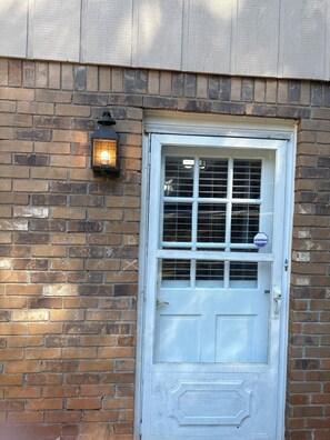 A white door with a window, a brick wall, and a wall-mounted light fixture.