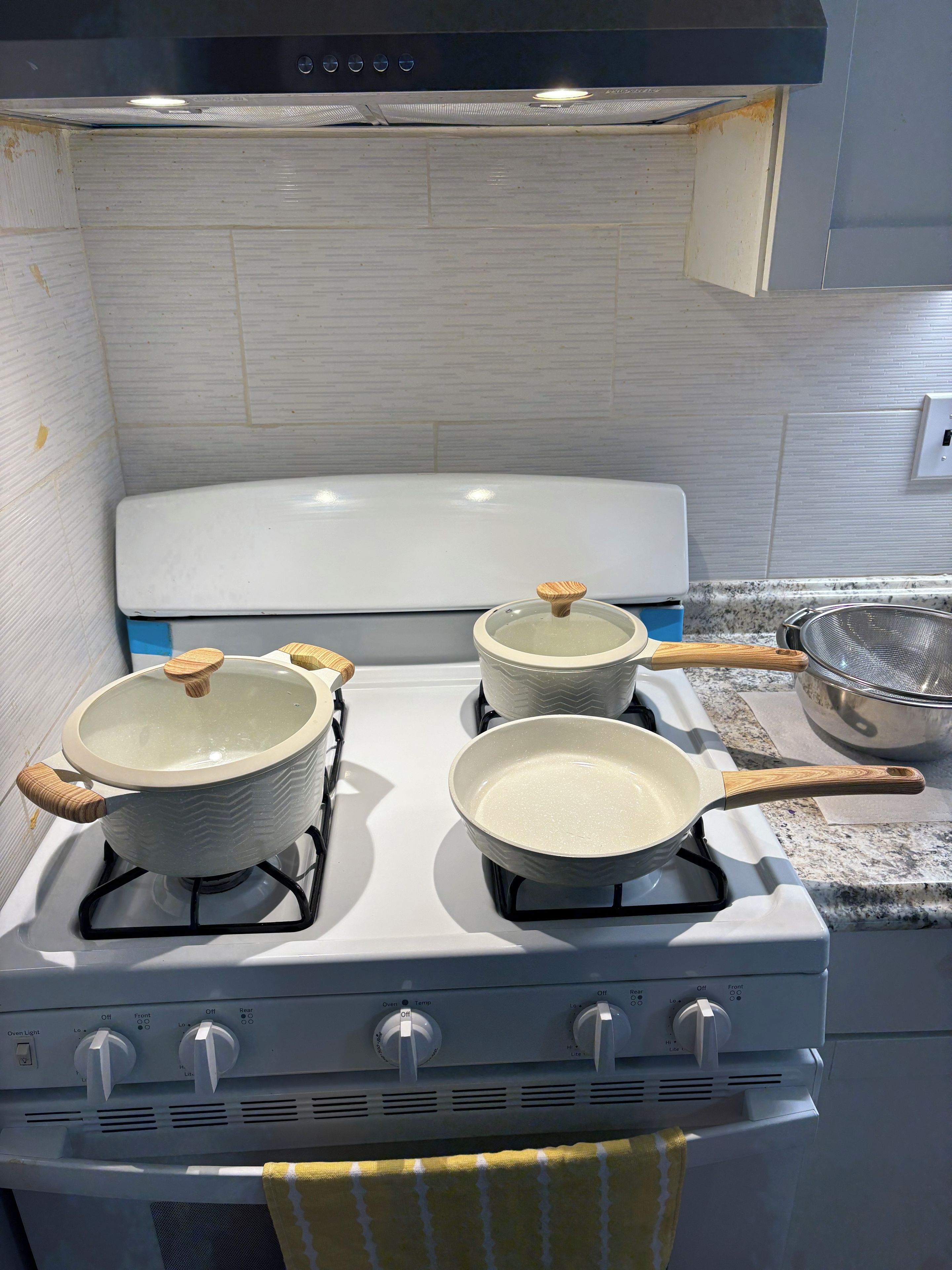 A kitchen with a white stove, three pots, and a strainer on the counter.