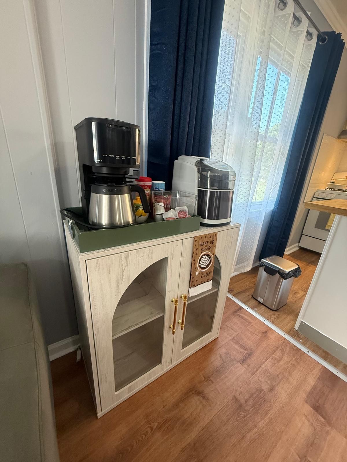 A kitchenette with a coffee maker, a kettle, and a trash bin.