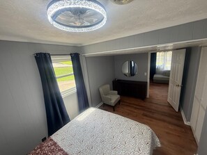 Ein Schlafzimmer mit Bett, Stuhl, Spiegel und Blick auf einen Garten durch ein Fenster.