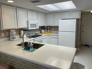 A modern kitchen with white cabinetry, a built-in microwave, a refrigerator, and a sink with a soap dispenser. - Coastal 2-BR Pet-Friendly Haven at Surfside 1 #210 - 2 Minutes to the Sand (South Padre Island)