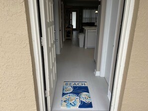 A hallway leading to a kitchen area with a door at the end. - Coastal 2-BR Pet-Friendly Haven at Surfside 1 #210 - 2 Minutes to the Sand (South Padre Island)