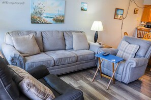 A living room with a grey sofa, a matching armchair, a blue side table, and a lamp. - Affordable 2-BR Escape at Surfside 1 #310 - 2 Minutes from the Sand (South Padre Island)