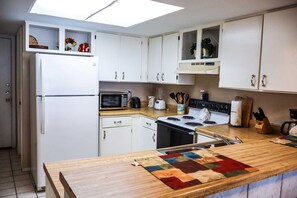 A kitchen with white cabinets, a microwave, a stove, and a wooden countertop. - Affordable 2-BR Escape at Surfside 2 #107 - Steps from the Sand (South Padre Island)