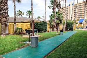 A pathway with green flooring, palm trees, and outdoor seating. - Affordable 2-BR Escape at Surfside 2 #107 - Steps from the Sand (South Padre Island)