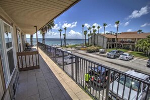 A balcony with a view of the ocean, a parking area, and a building with a red roof. - Sandcastle 201B - Affordable Bayside Efficiency Perfect for Small Families (South Padre Island)