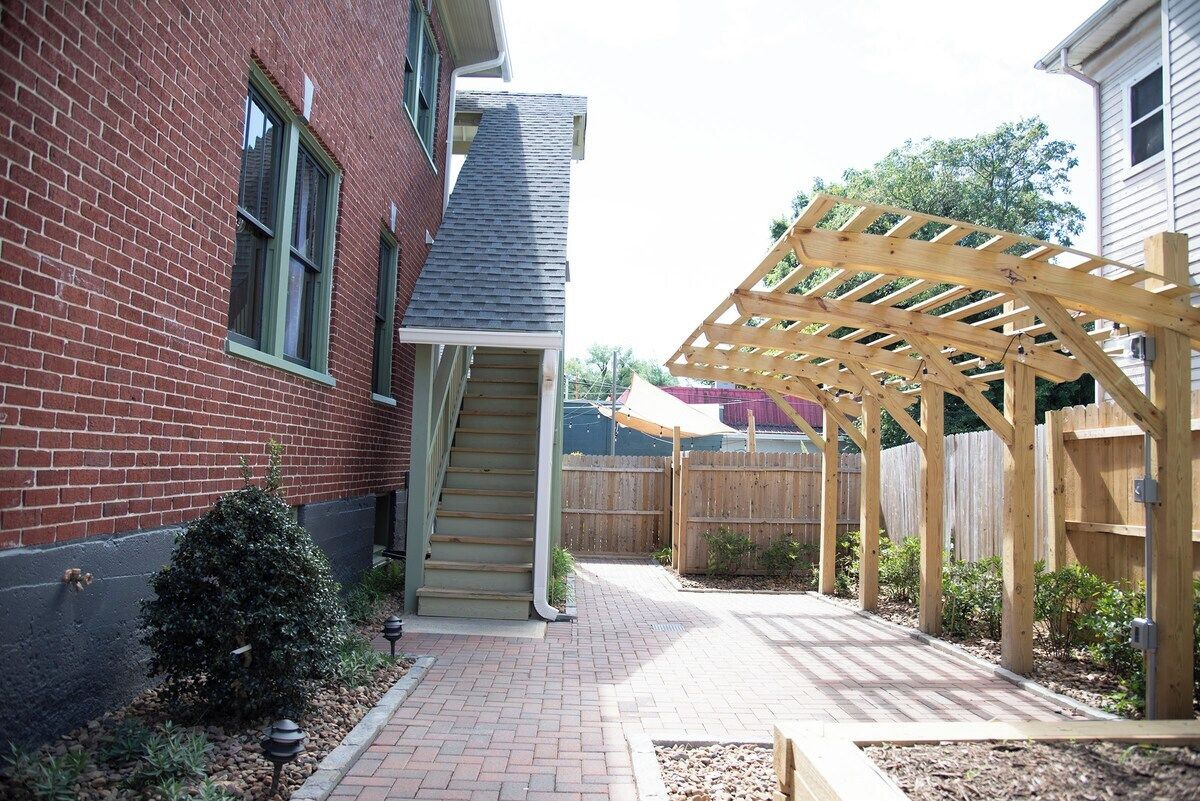 A brick house with a wooden pergola, a staircase, and a fenced backyard.
