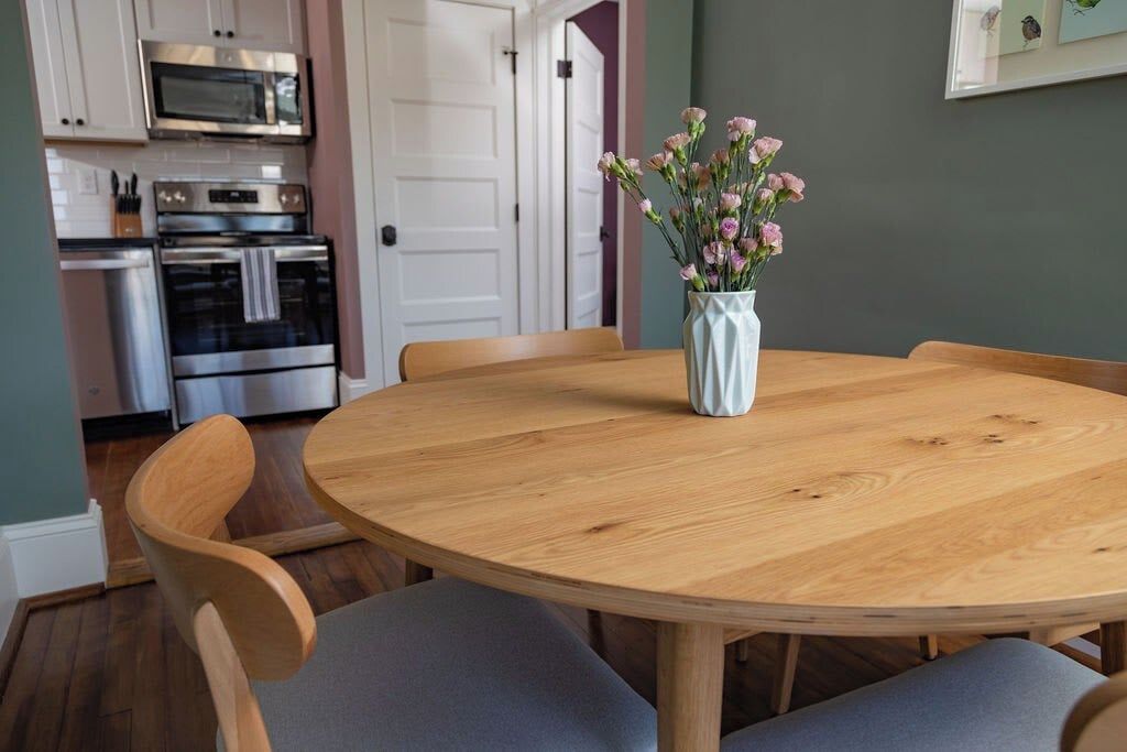 Un coin repas avec une table ronde en bois, quatre chaises et un vase rempli de fleurs.