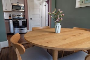 Un comedor con una mesa redonda de madera, cuatro sillas y un florero con flores.
