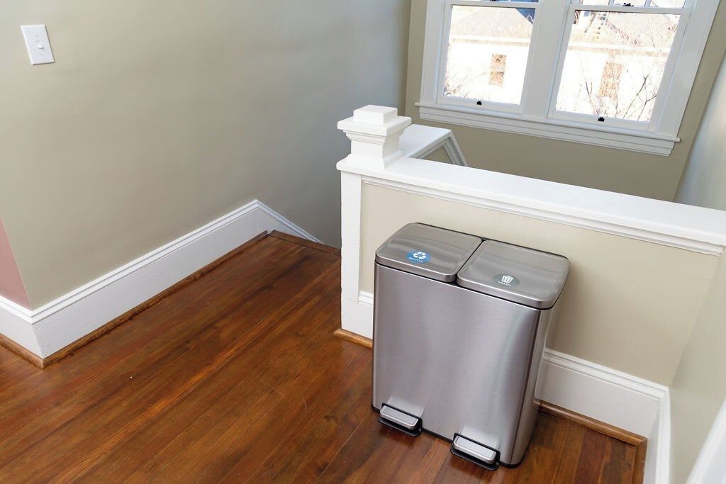 A room with a trash bin, wooden flooring, a window, and a white railing.