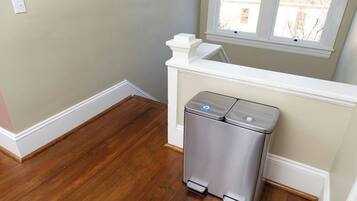 A room with a trash bin, wooden flooring, a window, and a white railing.