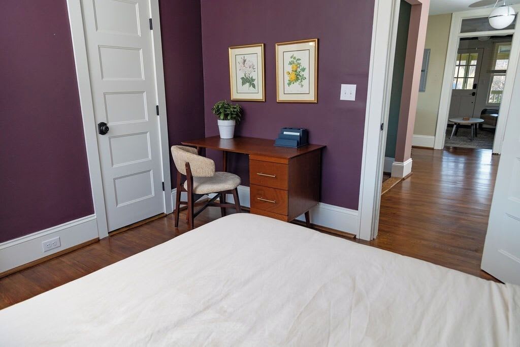 A bedroom with a bed, a desk, a chair, and two framed pictures on the wall.