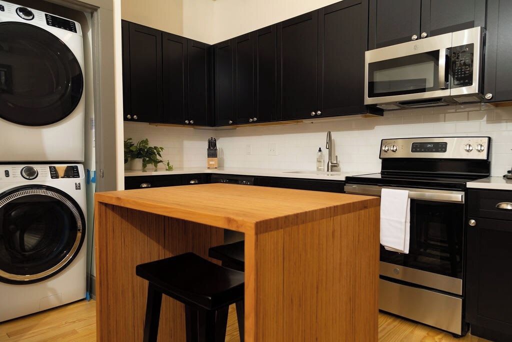 A compact kitchen with a built-in washer, a microwave, an oven, and a wooden island with a bench.