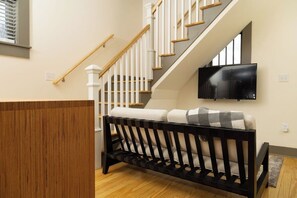 Eine Treppe mit weißen Geländern und Holzstufen, ein schwarzes Sofa mit einem karierten Kissen und ein an der Wand befestigter Flachbildfernseher.