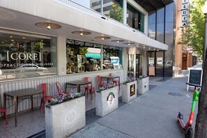 An outdoor seating area with tables and chairs, a storefront with a sign, and a scooter parked nearby. - Stay Roanoke | Chic downtown 1BR with study loft (Roanoke)