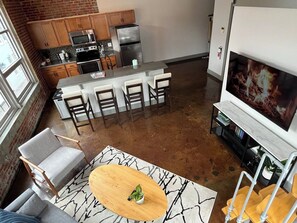 A modern kitchen with a central island, bar stools, and a large flat-screen TV mounted above the fireplace. - Stay Roanoke | Chic downtown 1BR with study loft (Roanoke)