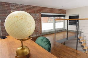 A globe on a wooden table in a room with a brick wall and a glass railing. - Stay Roanoke | Downtown Loft, Fast WiFi & Views (Roanoke)