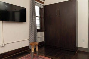 Een kamer met een donker houten garderobe, een wandgemonteerde flatscreen televisie, een houten kruk en een kamerbreed tapijt met een patroon.