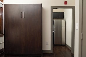 A room with a dark wooden wardrobe, a stainless steel refrigerator, and a kitchen area with cabinets. - Stay Roanoke | Stylish historic loft near downtown (Roanoke)