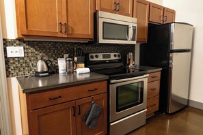 A kitchen with wooden cabinets, a stainless steel refrigerator, a microwave, an oven, and a coffee maker. - Stay Roanoke | Downtown Loft, Fast WiFi, City View (Roanoke)