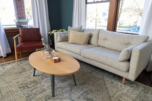 Ein Wohnzimmer mit einer Couch, einem Holztisch, einem roten Sessel und einem gemusterten Teppich.
