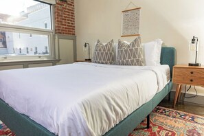 A neatly made bed with white bedding, a green headboard, and patterned pillows. - Stay Roanoke | Stylish 2BR downtown luxury (Roanoke)