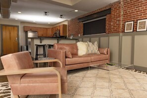 Ein modernes Wohnzimmer mit einer Ledersofa, einem Glastisch und einer Küchenzeile mit Holzausbau und einer Ziegelwand.