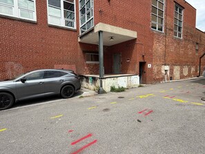 Ein Parkplatz mit einem Auto vor einem Backsteinhaus mit vielen Fenstern und einer Tür.