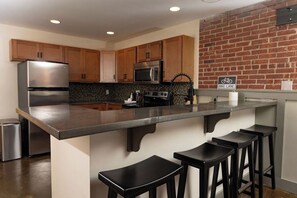 A kitchen with a central island, bar stools, stainless steel appliances, and a bike lane sign on the wall. - Stay Roanoke | Stylish 2BR downtown luxury (Roanoke)