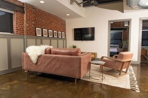 A modern living room with a leather sofa, a wooden chair, and a flat-screen TV mounted on the wall. - Stay Roanoke | Stylish 2BR downtown luxury (Roanoke)
