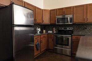 A kitchen with stainless steel appliances, wooden cabinets, and a tiled backsplash. - Stay Roanoke | Designer Loft w/Elevator, Fast WiFi (Roanoke)