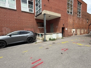 A parking area with a car parked by a brick building with multiple windows and a door. - Stay Roanoke | Designer Loft w/Elevator, Fast WiFi (Roanoke)