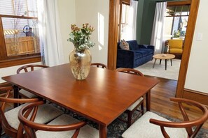 A dining area with a wooden table and chairs, a vase with flowers, and a view of a living room through an open door. - Stay Roanoke | Historic 2BR Near Dining & Trails (Roanoke)