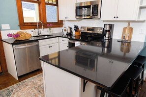 A modern kitchen with stainless steel appliances, a black countertop, and white cabinetry. - Stay Roanoke | Walkable 2BR Near Greenway (Roanoke)