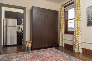 A room with a dark wooden wardrobe, a kitchen with a stainless steel refrigerator, and a patterned rug. - Stay Roanoke | Luxe loft w/city & mountain views (Roanoke)