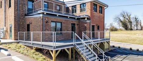 A multi-story building with a brick facade, a balcony, and a staircase leading to a lower level.