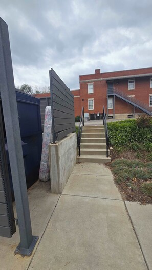 A concrete pathway leading to a building with a red brick facade and a staircase. - Stay Roanoke | Luxe loft w/city & mountain views (Roanoke)