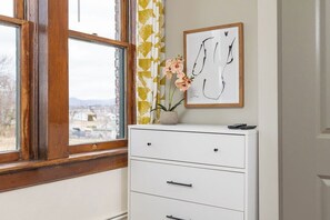 A room with a white filing cabinet, a framed abstract artwork, and a window with a view of a cityscape. - Stay Roanoke | Luxe loft w/city & mountain views (Roanoke)