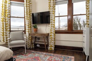 A room with a bed, a chair, a desk with a plant, a TV, and a dresser. - Stay Roanoke | Luxe loft w/city & mountain views (Roanoke)