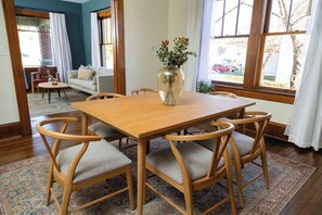 Ein Essbereich mit Holztisch und Stühlen, einer Vase mit Blumen und Blick durch große Fenster.