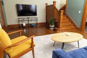 Ein Wohnzimmer mit Flachbildfernseher, einer Holztreppe und einem runden Couchtisch.