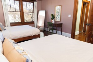 Une chambre avec deux lits, un bureau, une chaise et une fenêtre donnant sur des arbres.