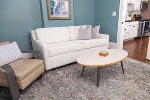 Uma sala de estar com um sofá branco, uma mesa de centro redonda e um tapete estampado.