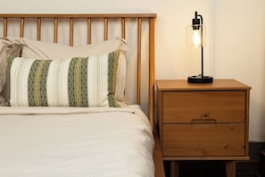 Ein Bett mit Holz-Kopfteil, einer Nachttischlampe und einem Nachttisch mit Schubladen.