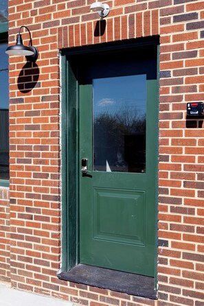 Eine grüne Tür mit kleinem Fenster, einem Briefkasten und einer Wandleuchte.